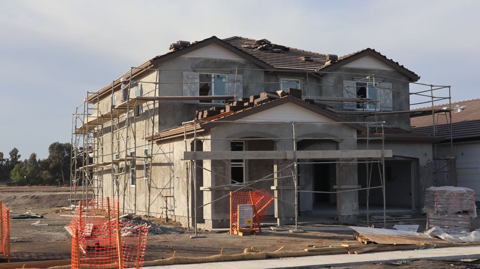 A modern two-story house under construction with visible scaffolding and building materials.